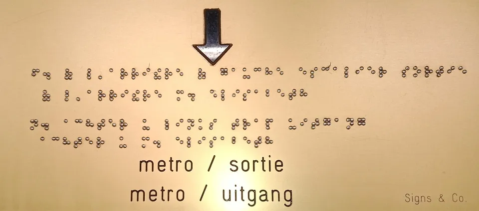 A bilingual sign with braille text and arrows for the metro exit