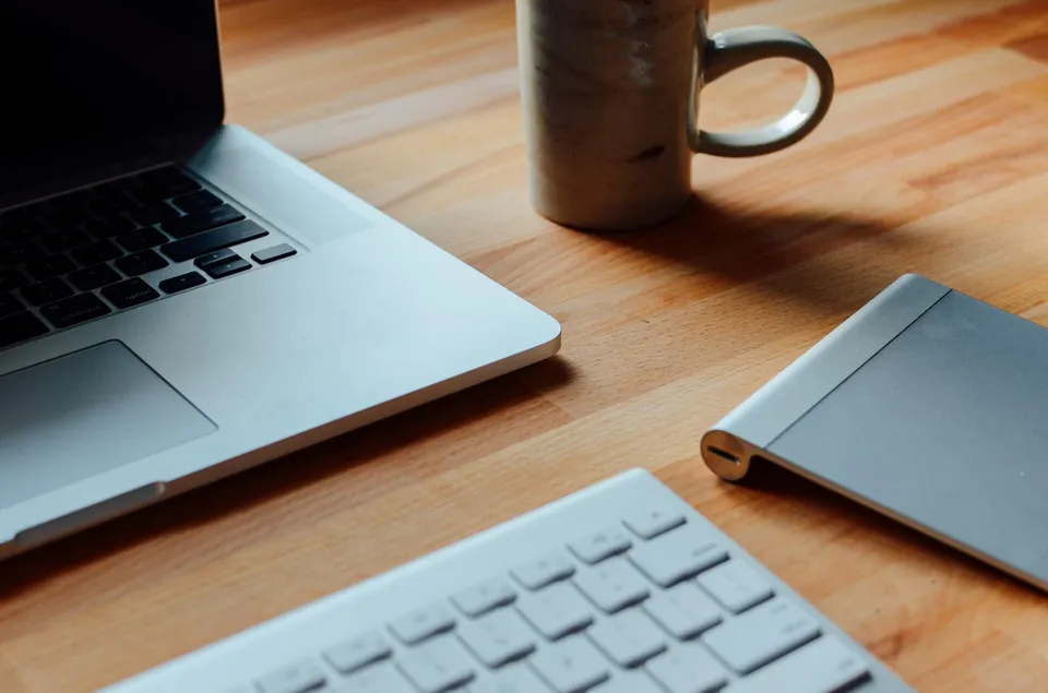 Close-up of a laptop keyboard and a coffee mug on a wooden desk