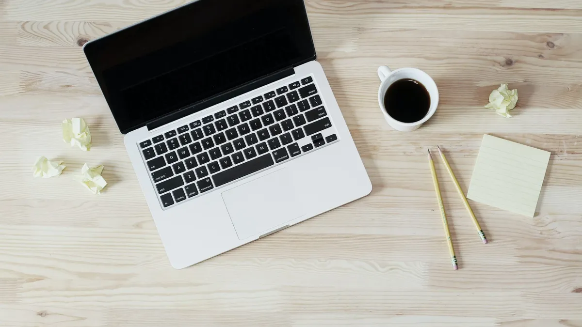 An open laptop and a cup of coffee on a light wooden desk, seen from above