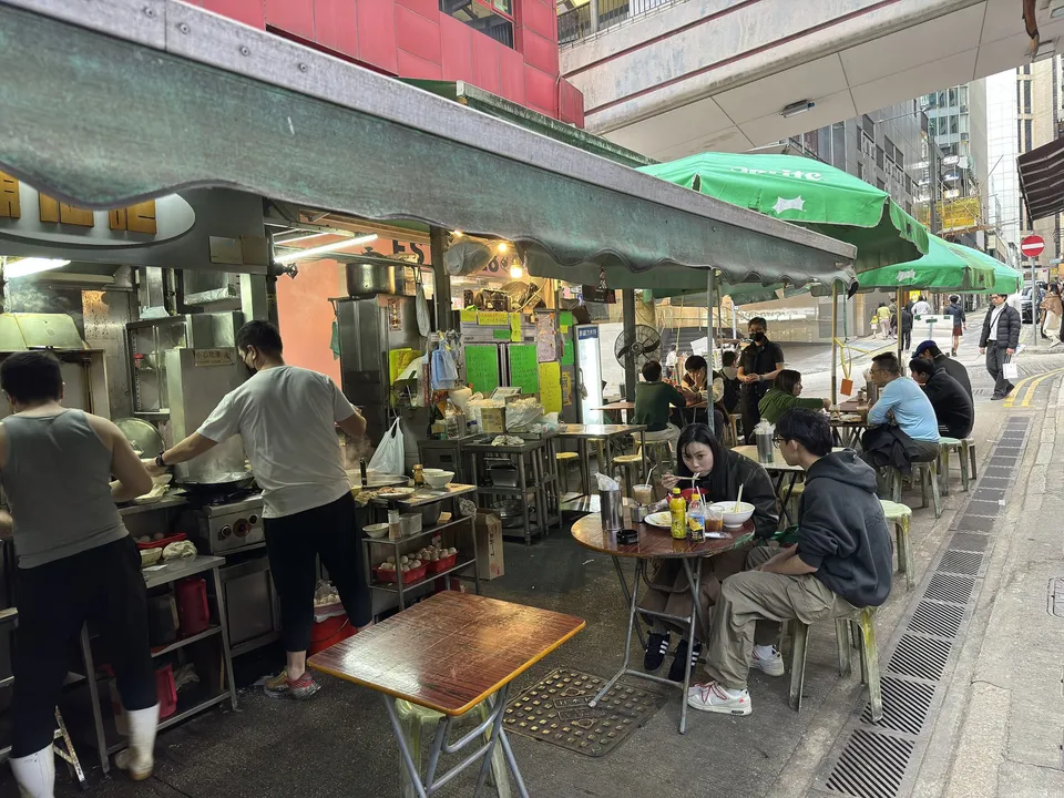 Cooks at work beside folding tables under a canopy in a Central lane