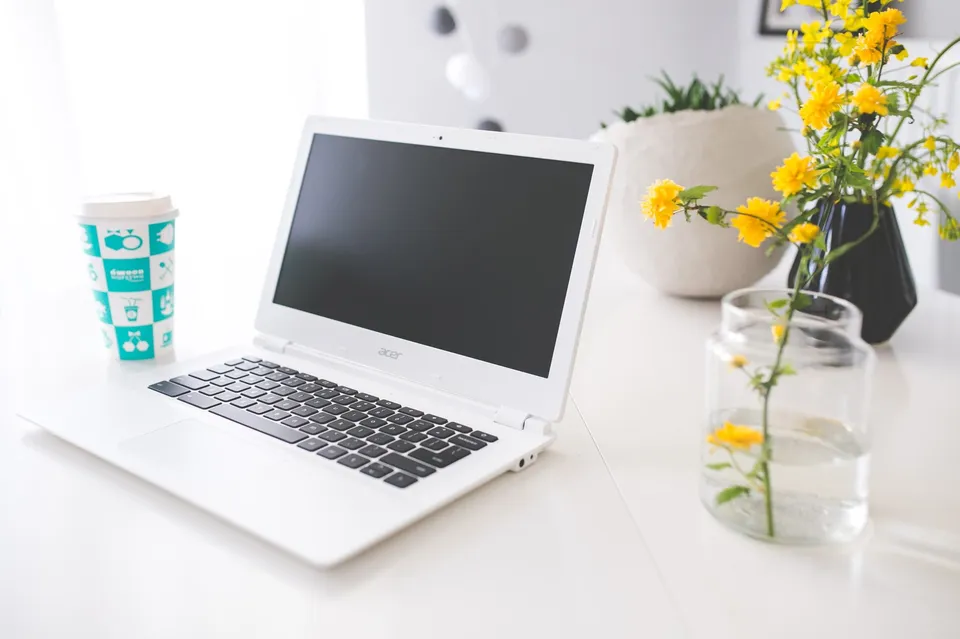 A laptop and notebook on a clean desk beside a cup of coffee