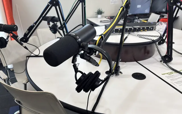 Broadcast microphones on boom arms around a round studio table