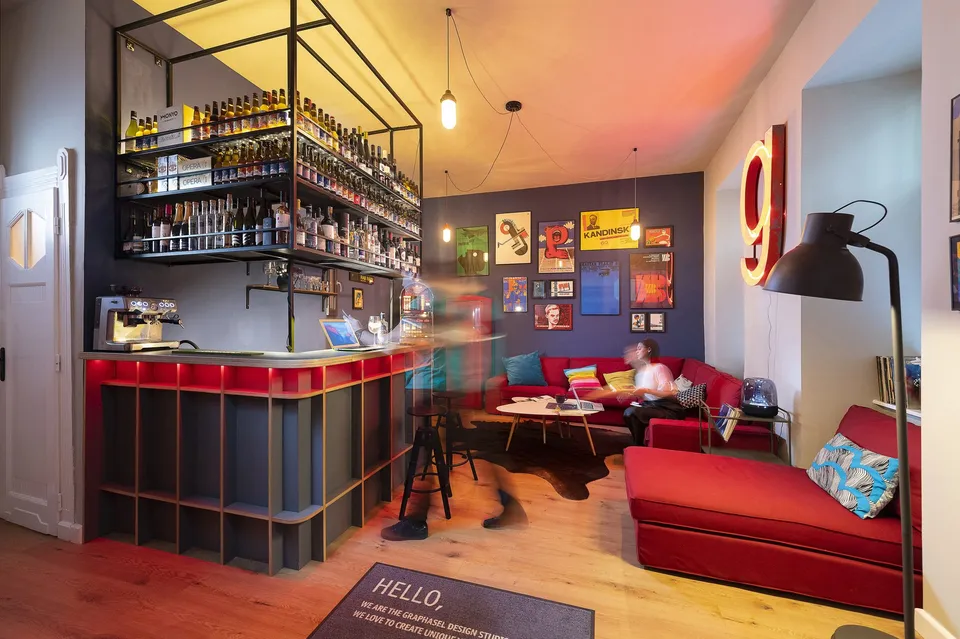 A studio lounge with framed posters, a red sofa and a small bar