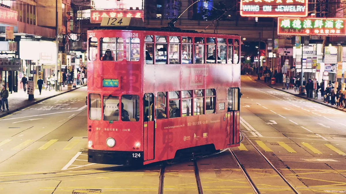 A red double-decker tram at night on a wide street lined with neon signs